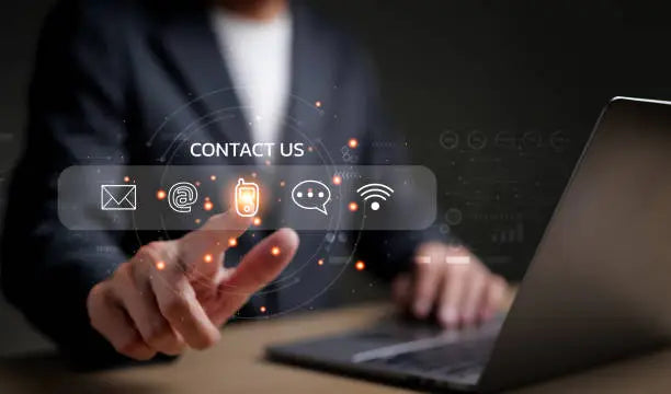 A person in a suit interacts with a holographic "Contact Us" interface featuring icons for email, call, chat, and Wi-Fi, set against a dark background.
